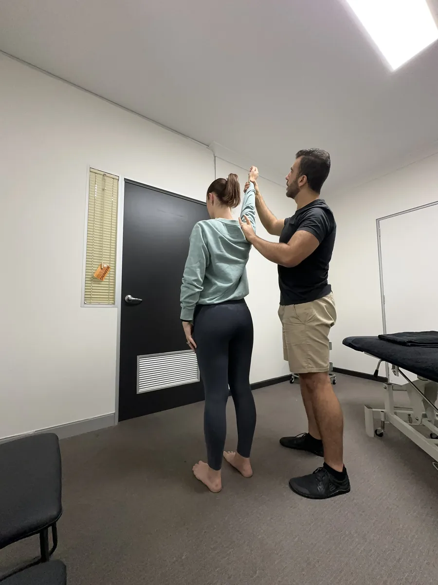 Osteopath Steven Eskaf assessing a standing patient’s shoulder and arm range of motion in the Berwick clinic